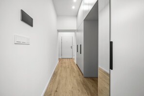 A modern hallway with white walls, a wooden floor, and a door at the end. - 1 room apartment with garden, Nálepkova 1390 (Liptovský Mikuláš)
