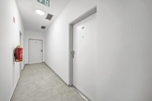 A corridor with a fire extinguisher on the left, a door with the number 105 on it, and a ceiling vent. - 1 room apartment with garden, Nálepkova 1390 (Liptovský Mikuláš)