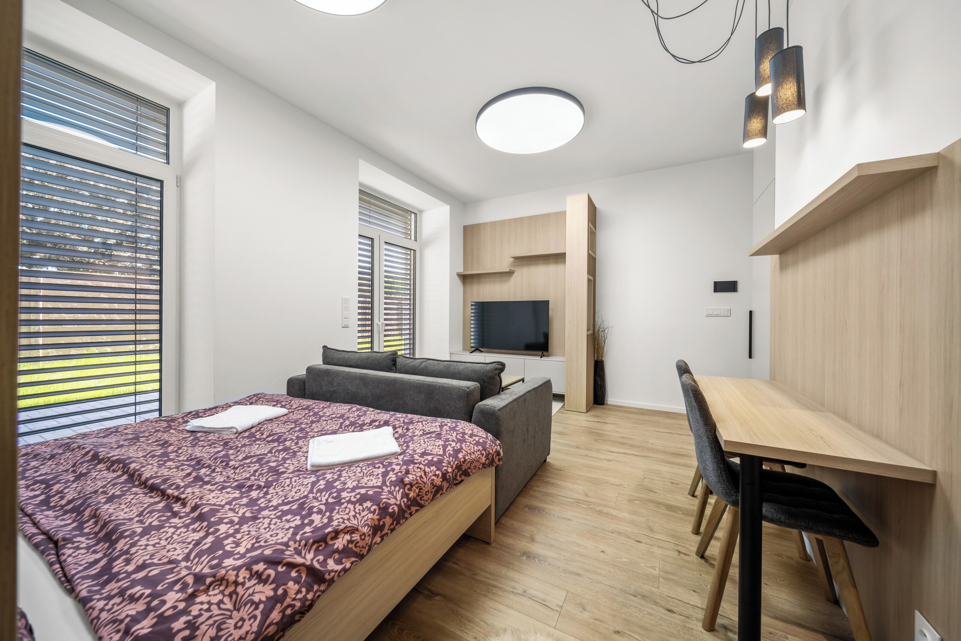 A modern bedroom with a bed, a desk, and a TV.