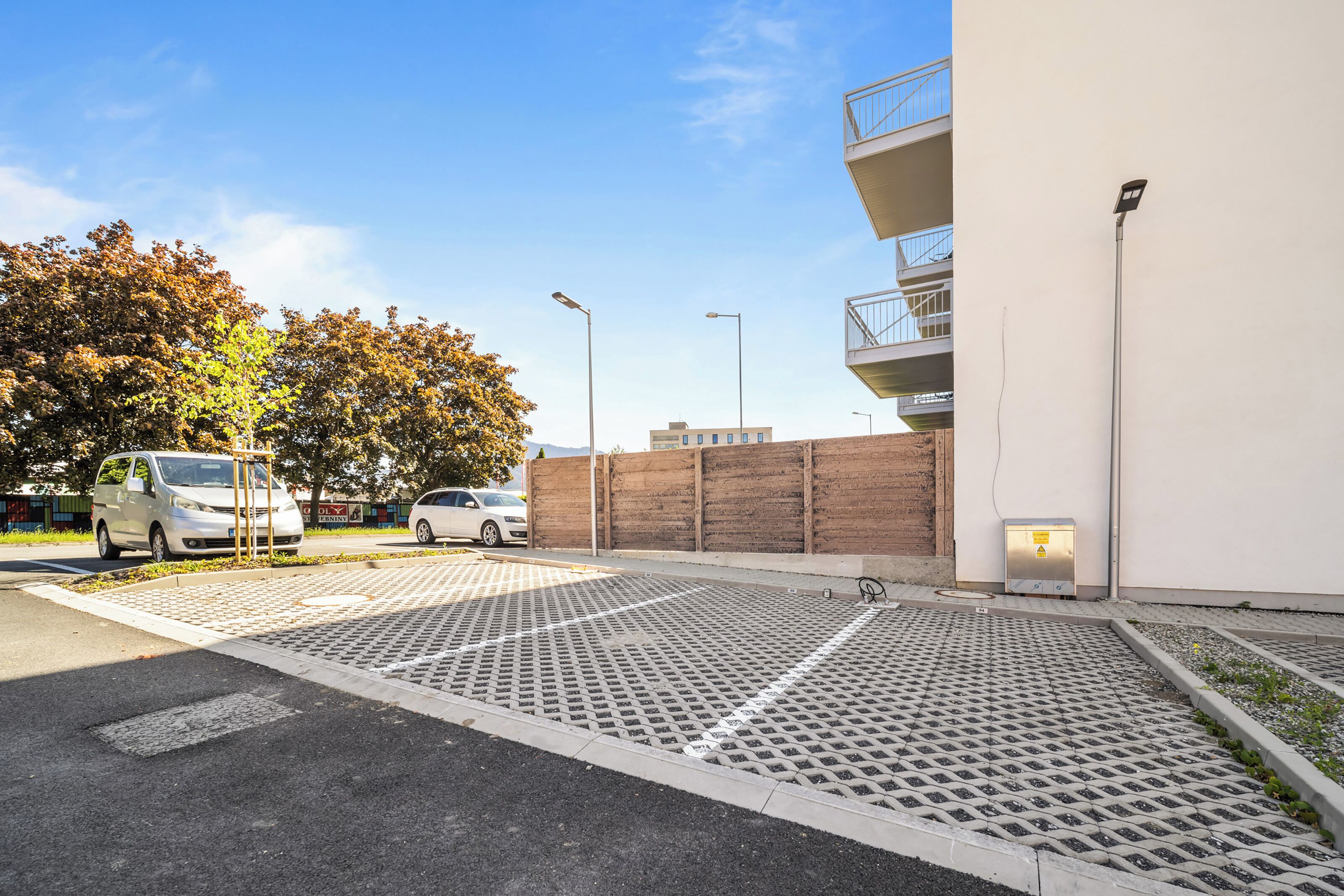 A parking area with a white building, a brick wall, and trees with autumn leaves.