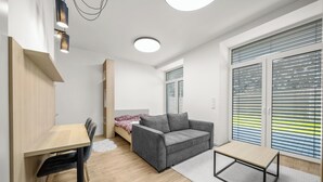 Ett modernt, väl upplyst rum med en säng, en grå soffa, ett litet bord och ett skrivbord.