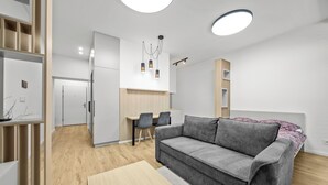 Ett modernt vardagsrum med en grå soffa, trägolv och en matplats med ett bord och stolar.