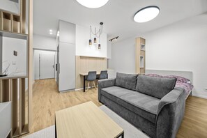 Ein modernes Wohnzimmer mit grauem Sofa, Holzboden und einem Essbereich mit Tisch und Stühlen.
