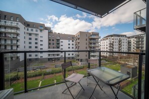 En balkong med ett glasbord och stolar, med utsikt över ett bostadsområde med flera hyreshus.