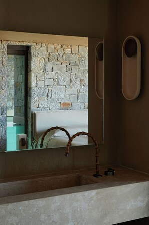A bathroom with a stone wall, a sink with a wooden faucet, and a mirror reflecting the room. - The Tierras - Ryāki | One Bedroom Private Pool Villa (Mononaftis)