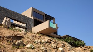 Um edifício moderno com fachada de pedra, uma varanda com guarda-corpo de vidro e um céu azul claro.