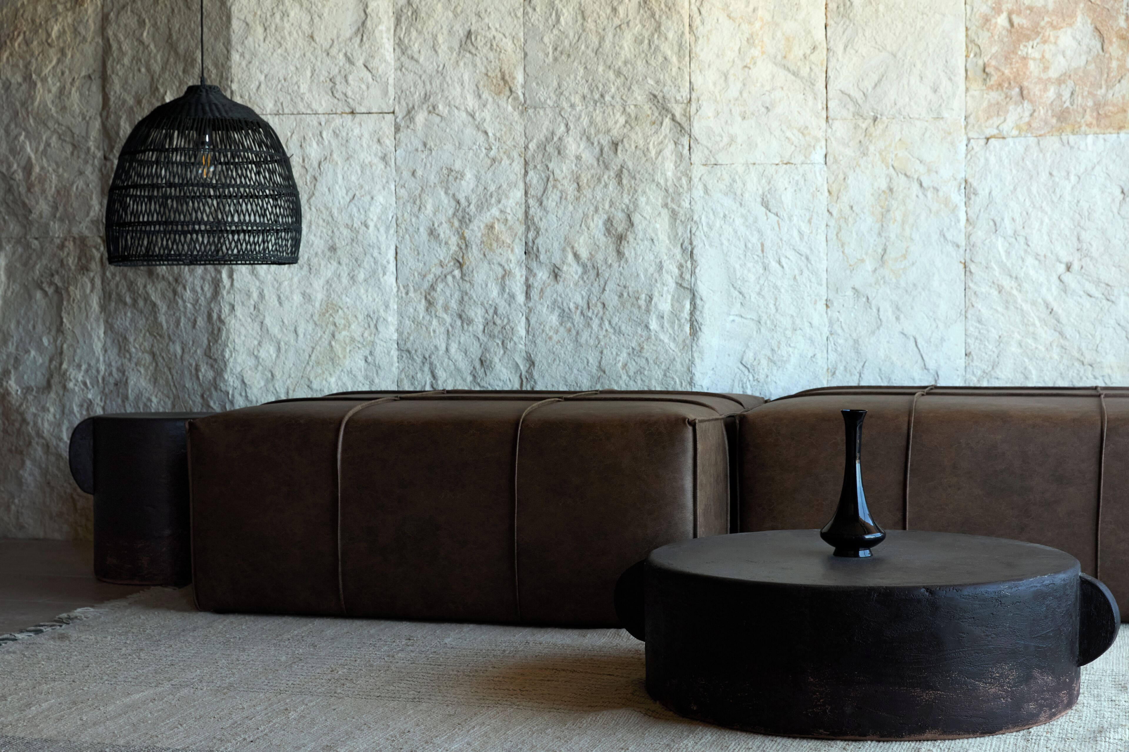 A sectional sofa with a round coffee table in a room with a textured wall and a hanging light fixture.