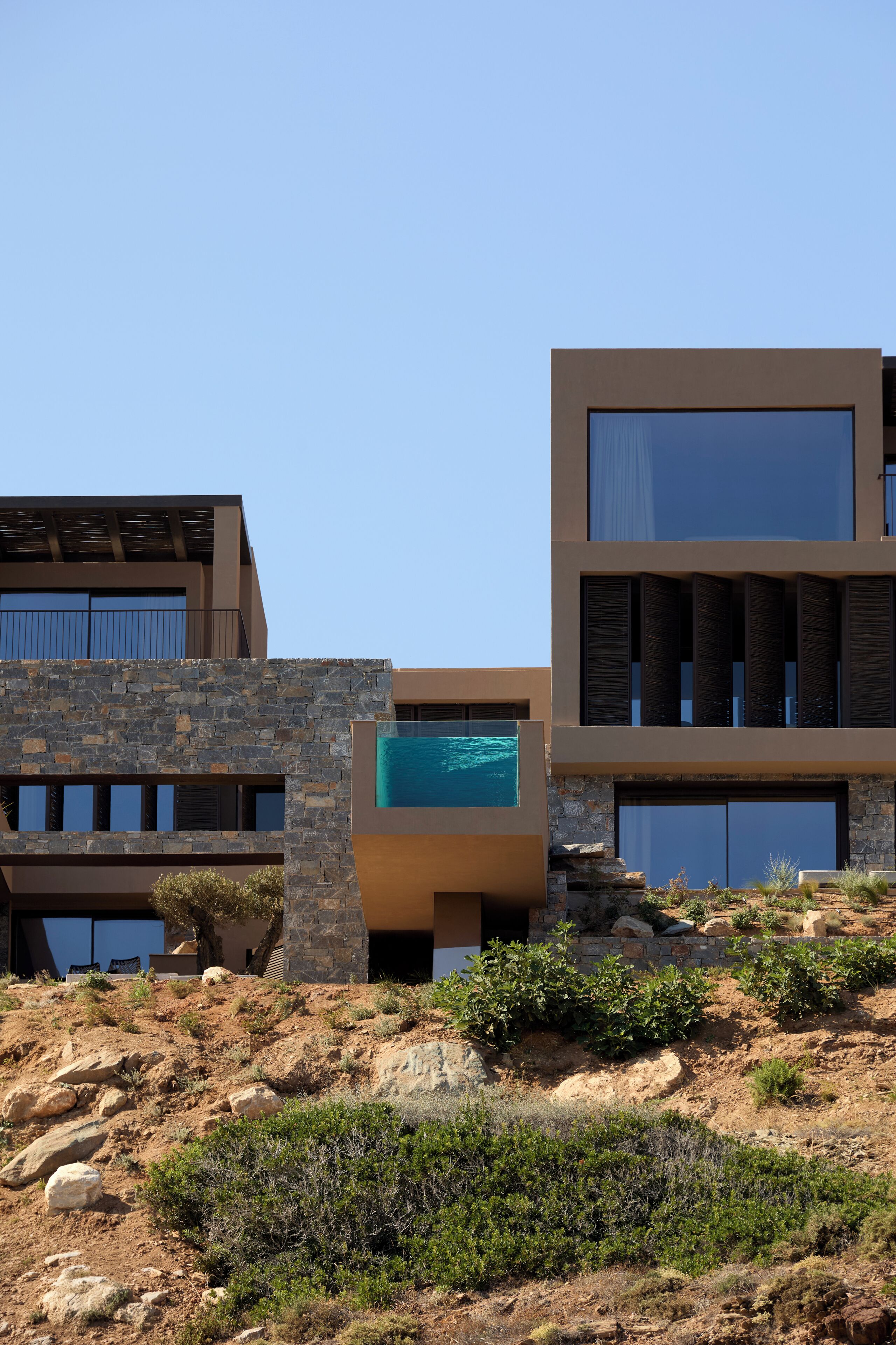 A modern building with a stone facade, a swimming pool, and a desert landscape.