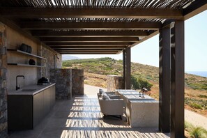 An outdoor kitchen area with a stone wall, a sink, and a built-in grill. - The Tierras - Ryāki | One Bedroom Private Pool Villa (Mononaftis)
