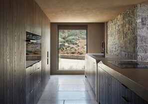 Eine moderne Küche mit Holzschränken, einer Steinrückwand und Blick auf eine angelegte Außenanlage.