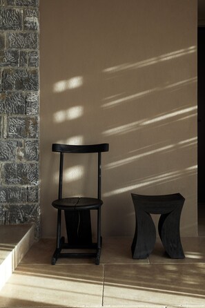 Una habitación con pared de piedra, una silla de madera y una pequeña mesa.