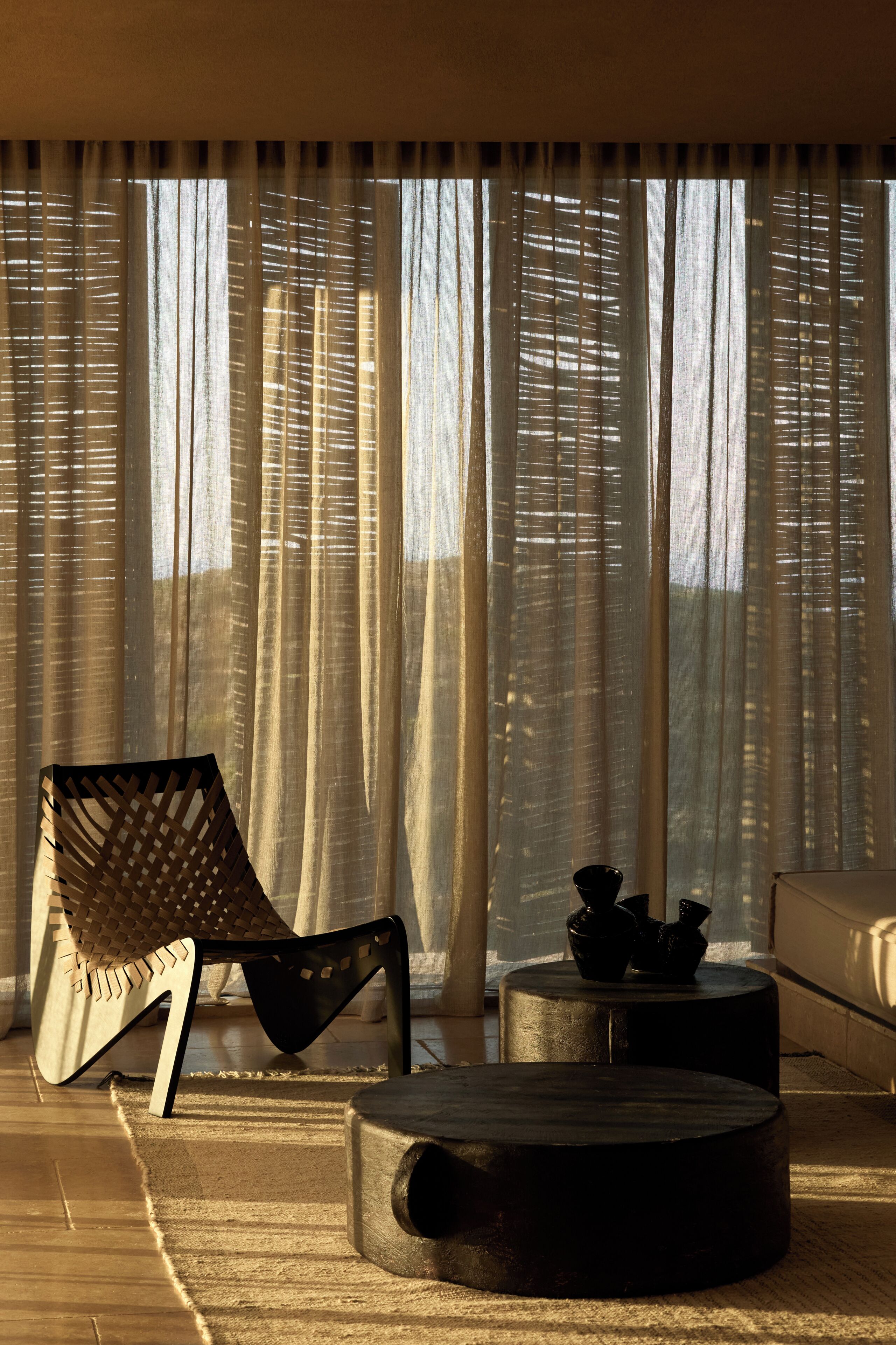 A modern living room with a large window, a woven chair, a round coffee table, and a sofa.