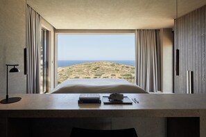 A bedroom with a large window, a bed, a desk with a lamp, and a view of a desert landscape. - The Tierras - Phōs | 2 Bedroom Maisonette Private Pool Villa (Mononaftis)