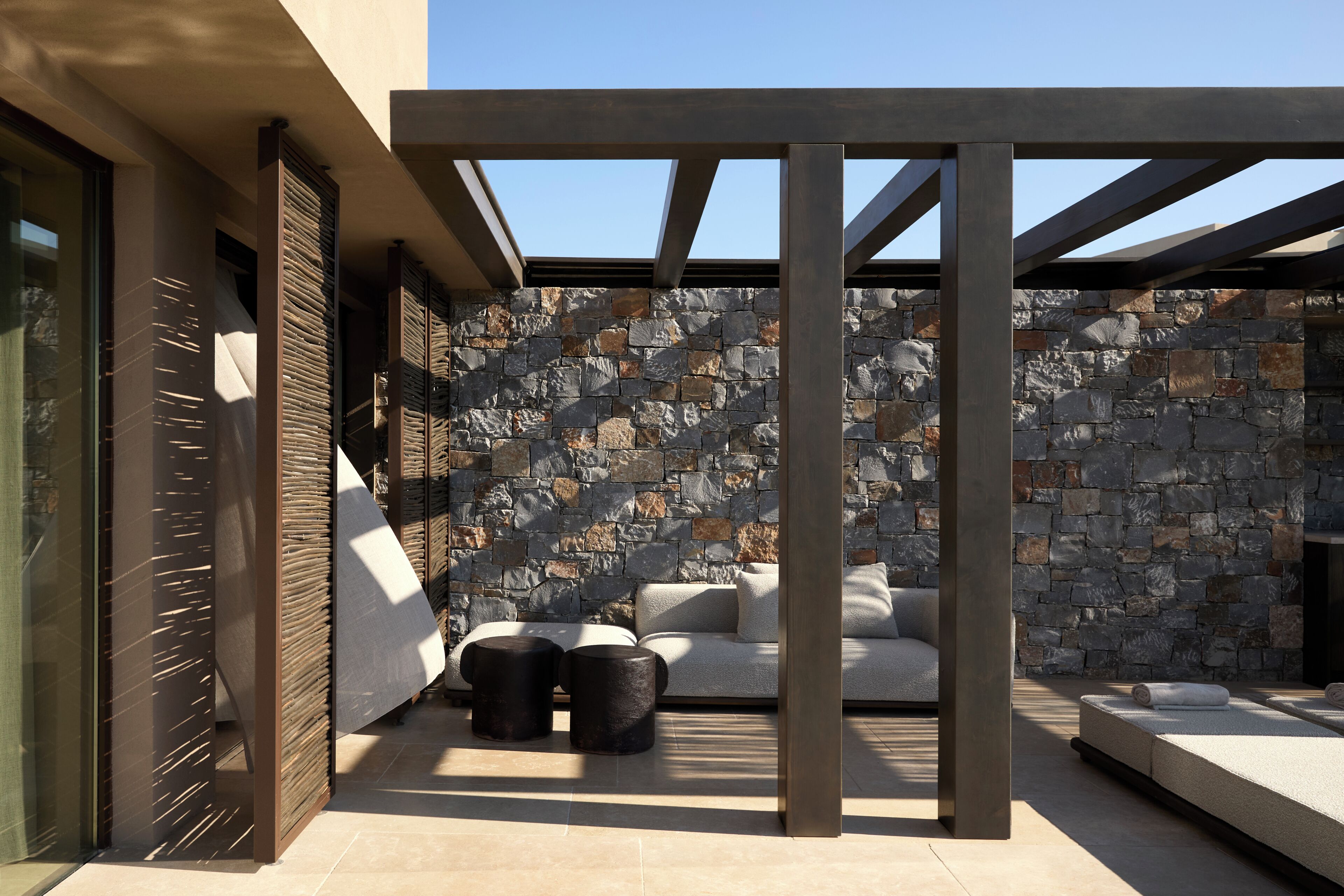 Un área de estar al aire libre moderna, con muros de piedra y vigas de metal.