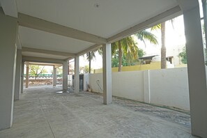 Un espacio interior cubierto con suelo de concreto, paredes blancas y vistas a palmeras y una pared amarilla en el exterior.