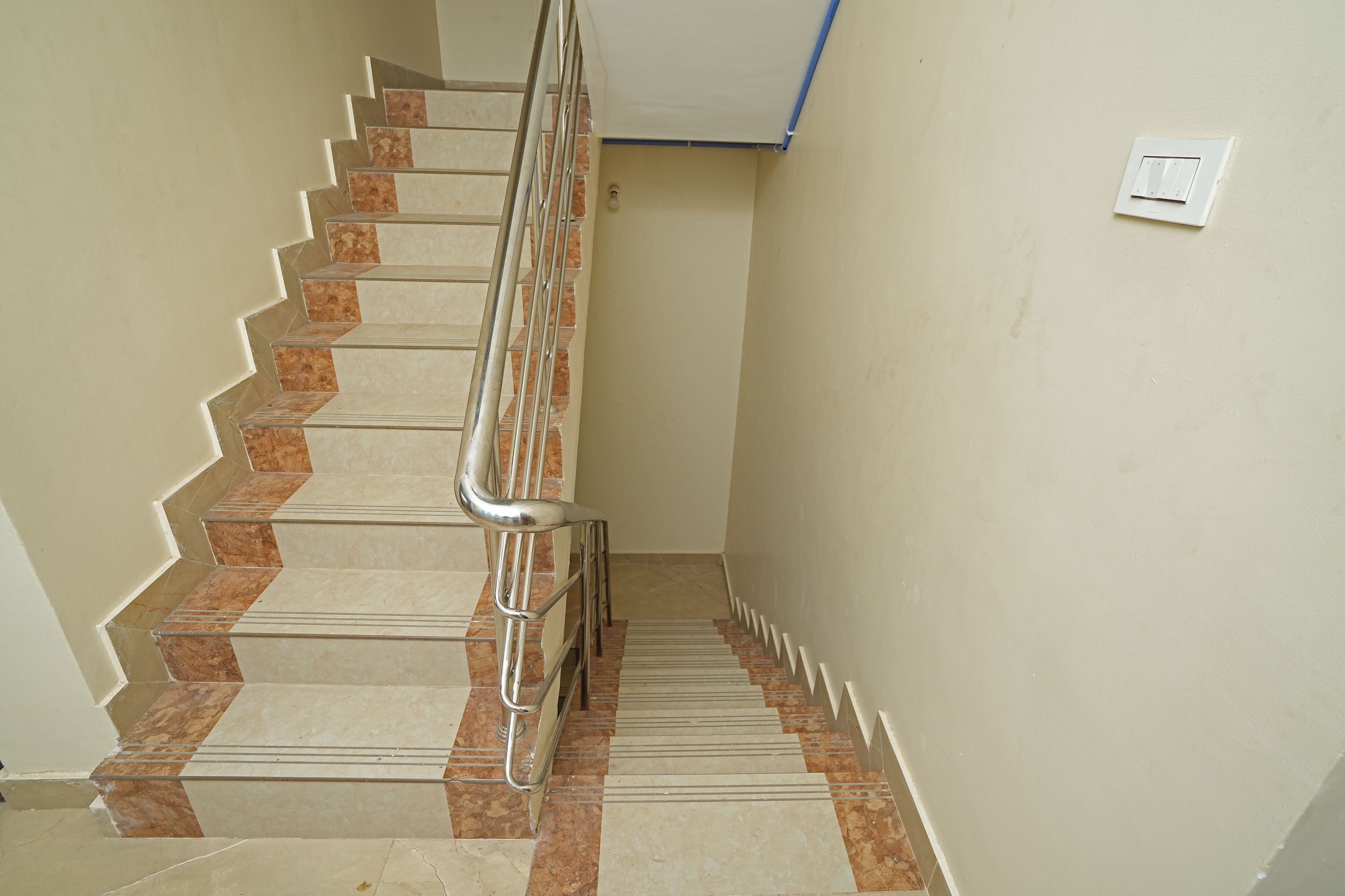 A staircase with a handrail, marble steps, and a light switch on the wall.