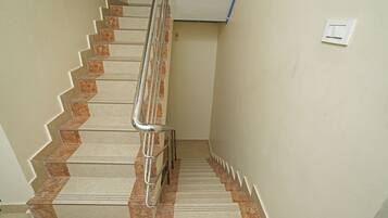 A staircase with a handrail, marble steps, and a light switch on the wall.