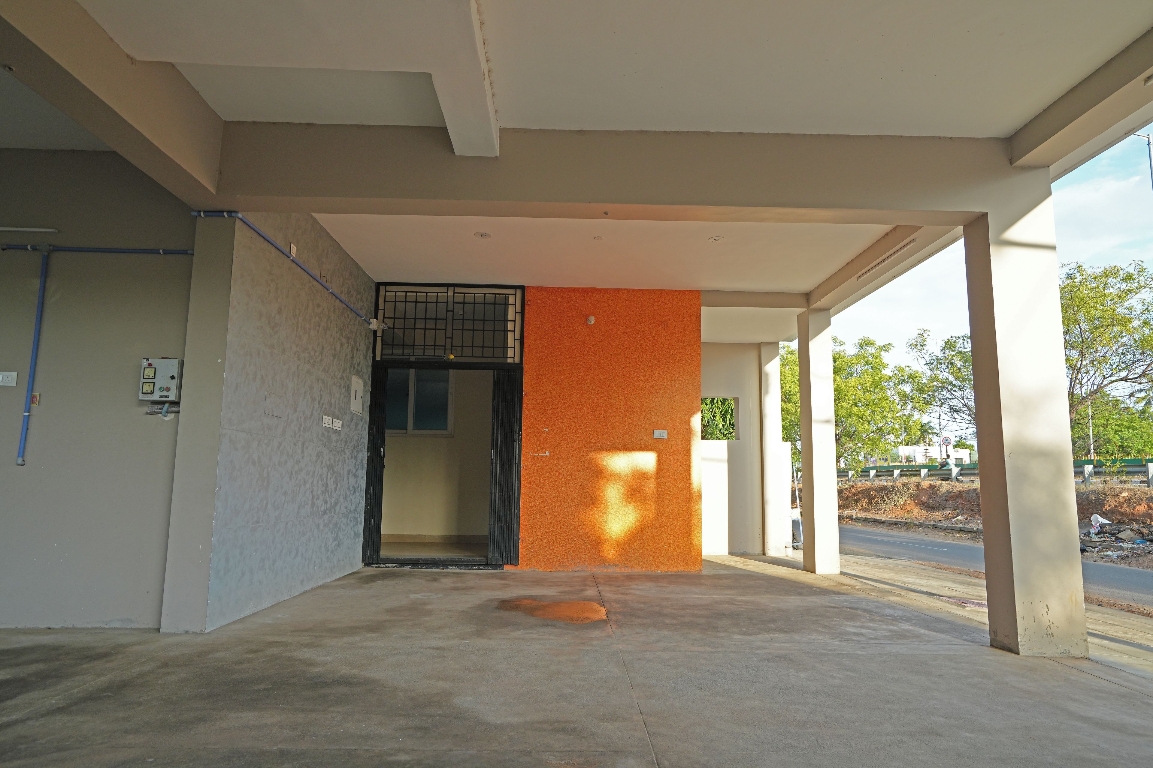 An indoor area with a concrete floor, a door leading to a room, and a wall with a textured orange surface.