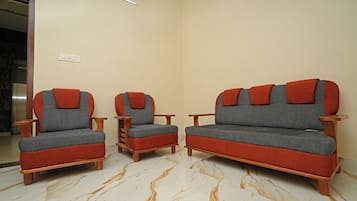 A room with two sofas and a chair, a marble floor, and a light switch on the wall.