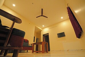 Una habitación con ventilador de techo, una silla roja, una mesa de madera y un televisor montado en la pared.