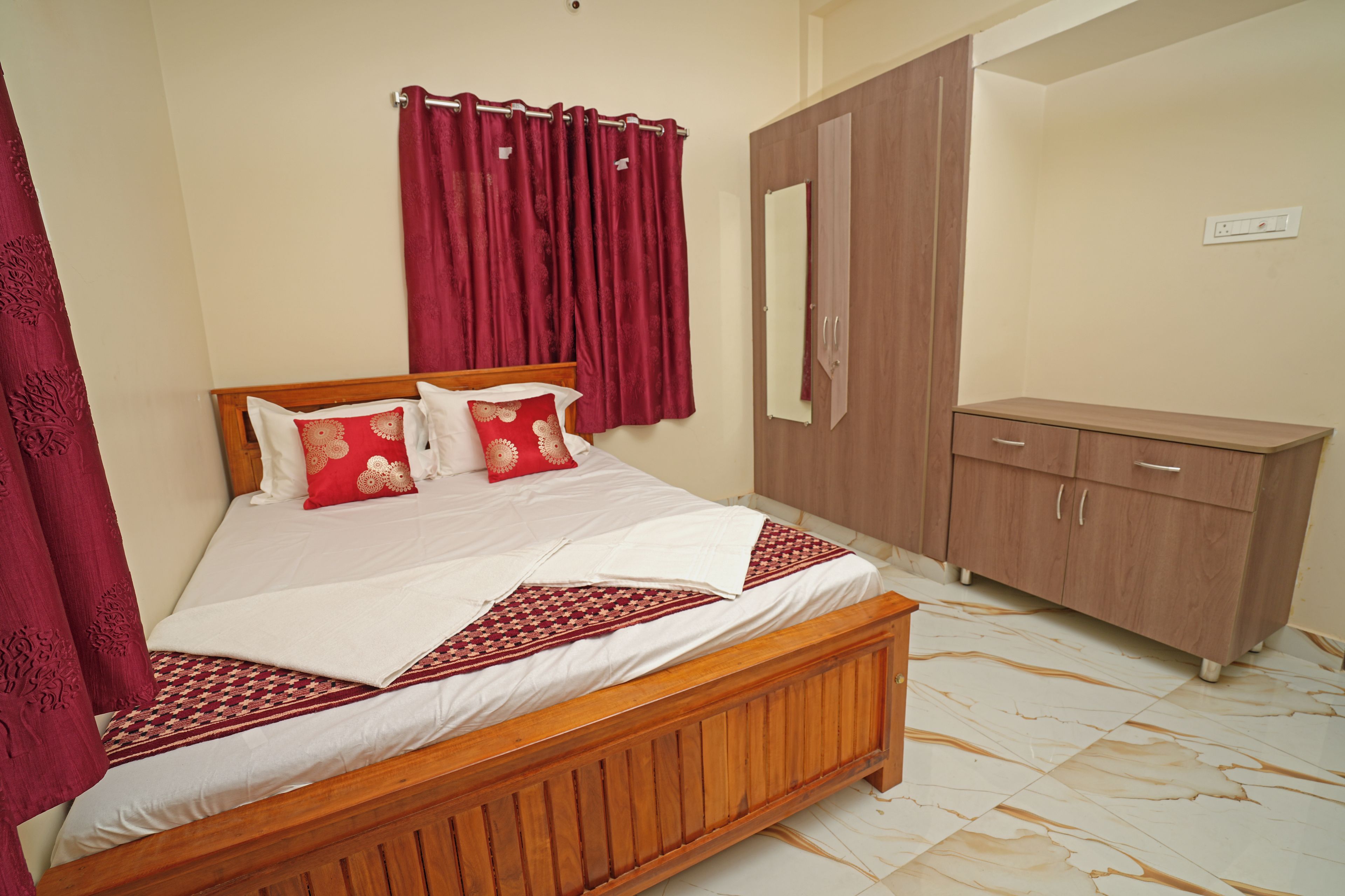 A bedroom with a wooden bed, red curtains, a wardrobe, and a mirror.