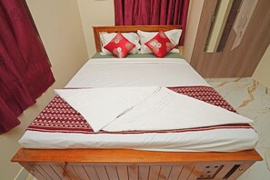 A neatly made bed with white and red bedding, a wooden headboard, and a red curtain.
