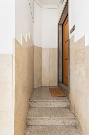 Eine enge Treppe mit einer Holztür am oberen Ende und einer Fußmatte auf den Stufen.