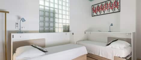 Una habitación con dos camas, una ventana con vistas, un cuadro en la pared y un escritorio con una lámpara.