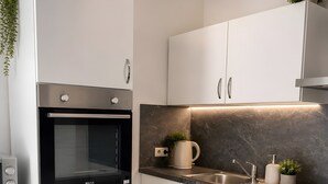 Uma cozinha moderna com armários brancos, forno embutido, painel de fundo de mármore e pia de aço inoxidável.