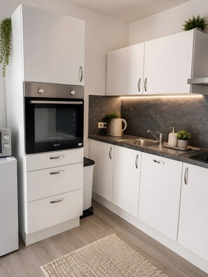 Eine moderne Küche mit weißen Schränken, einem eingebauten Backofen, einer Marmor-Spritzschutzwand und einer Edelstahl-Spüle.