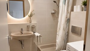 Um banheiro moderno com pia, espelho, vaso sanitário, chuveiro e máquina de lavar.