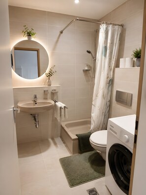 Ein modernes Badezimmer mit Waschbecken, Spiegel, Toilette, Dusche und einer Waschmaschine.