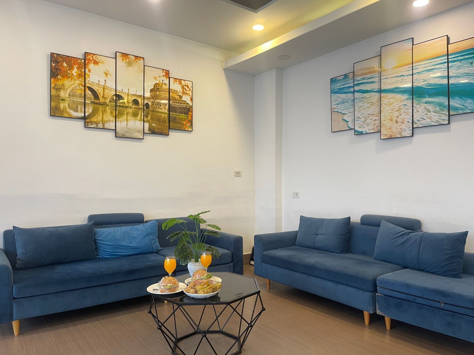 A modern living room with two blue sofas, a coffee table, and artwork on the walls.