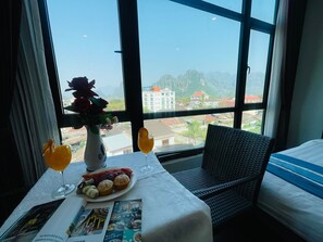 A hotel room with a large window, a table with a vase of flowers, a plate with fruit, and a magazine. - Hotel RainBow Boutique Vang Vieng (Vang Vieng)