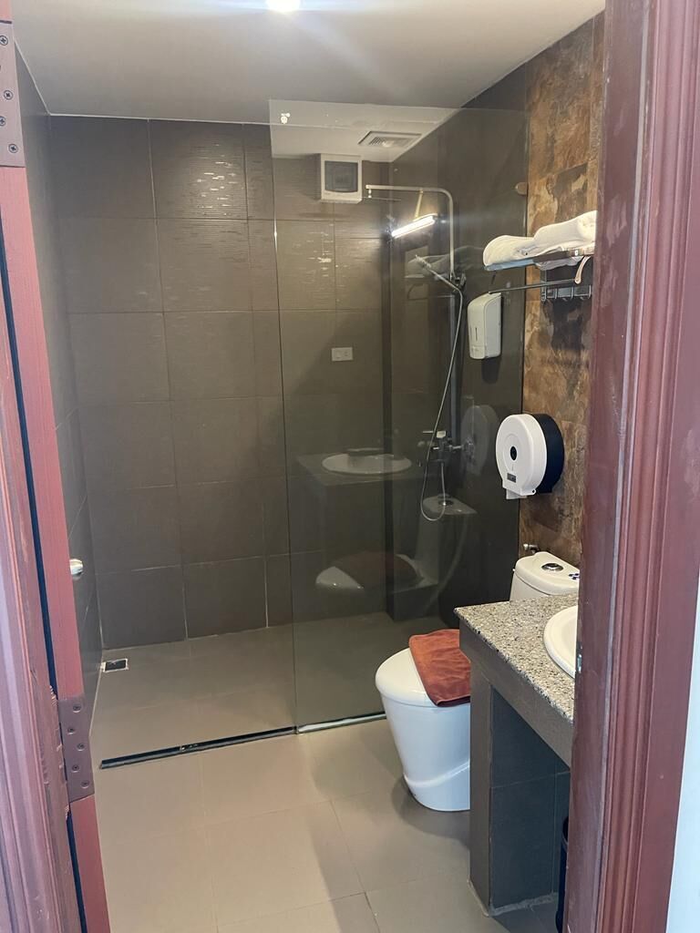 A bathroom with a glass-enclosed shower, a toilet, and a sink with a towel dispenser.