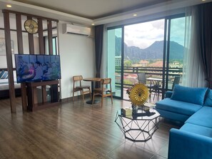Una habitación de hotel moderna con un ventanal grande, televisión, sofá y zona de comedor.