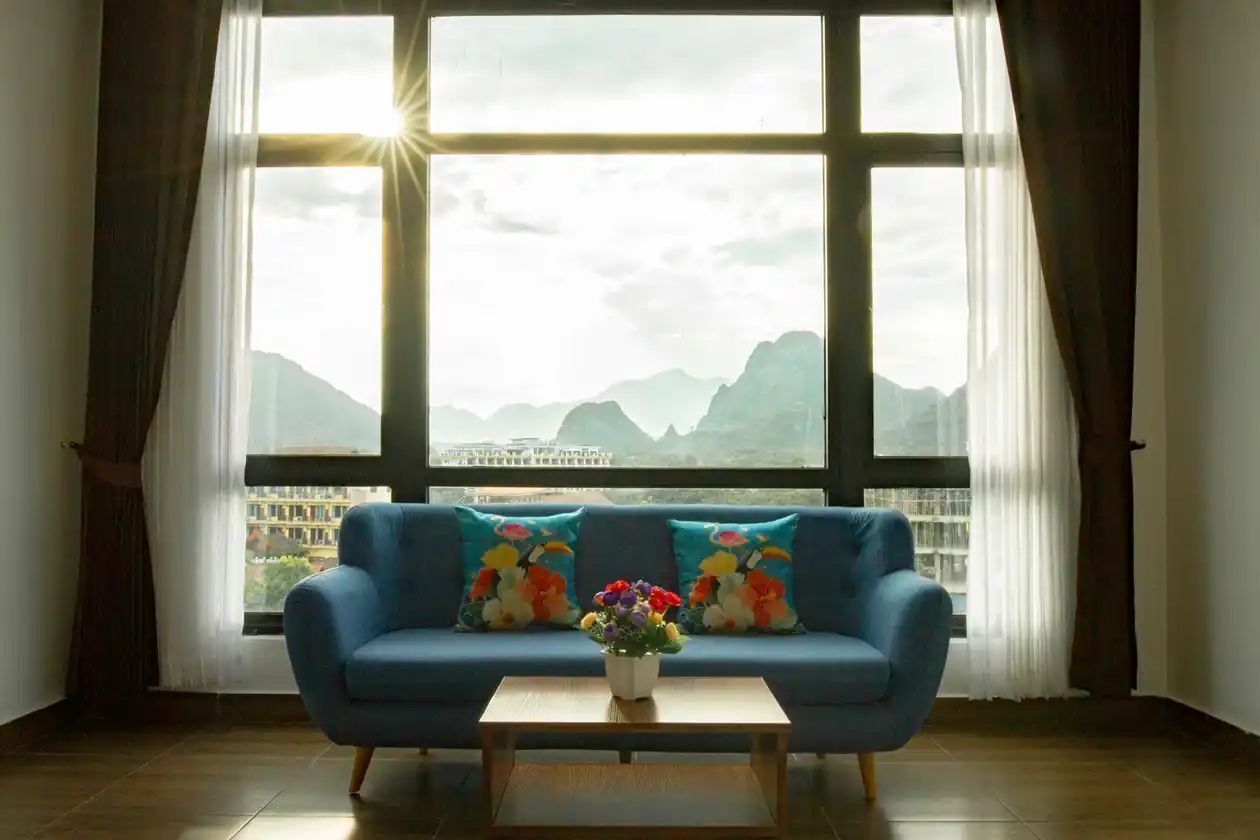 A room with a blue sofa, a coffee table, and a window with a view of mountains.