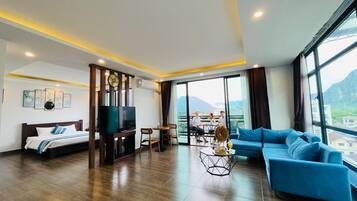 A modern hotel room with a bed, a TV, a sofa, and a balcony with a view of the mountains.