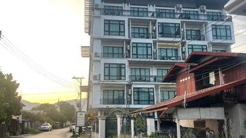 A multi-story building with balconies, a gated entrance, and a road in the foreground.