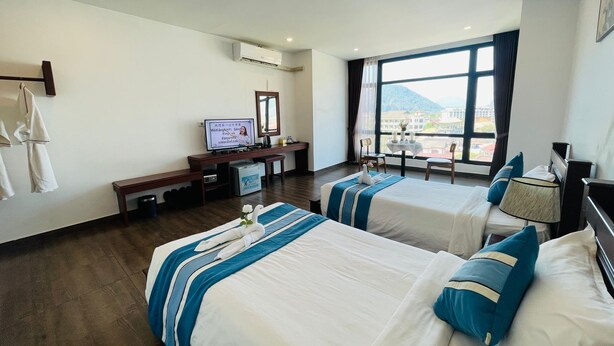 Habitación de hotel con dos camas, un escritorio, un televisor y un amplio ventanal con vistas.