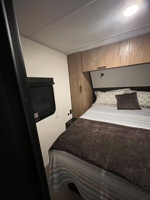 A compact RV bedroom with a bed, a headboard, and a window. - In the country Fishing hunting boating kayaking. (Mercer)