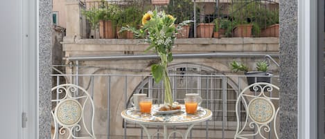A balcony with a table set for two, featuring a vase with flowers and two cups of orange juice.