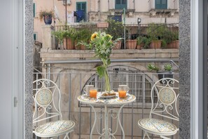 Ein Balkon mit Tisch für zwei Personen, eine Vase mit Blumen und zwei Gläser Orangensaft.