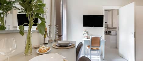 Un comedor con una mesa dispuesta para dos personas, un florero con flores y un televisor al fondo.
