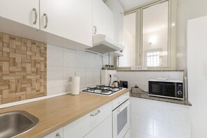 Eine moderne Küche mit weißen Schränken, einer Holzrückwand, einem Gasherd, einer Mikrowelle und einem Fenster über der Spüle.