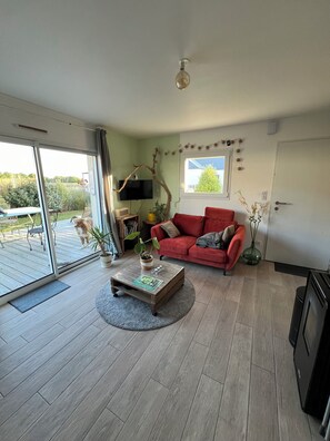 A living room with a red sofa, a coffee table, a TV, and a sliding glass door leading to a patio. - Beachfront Rental Home (Ploubalay)