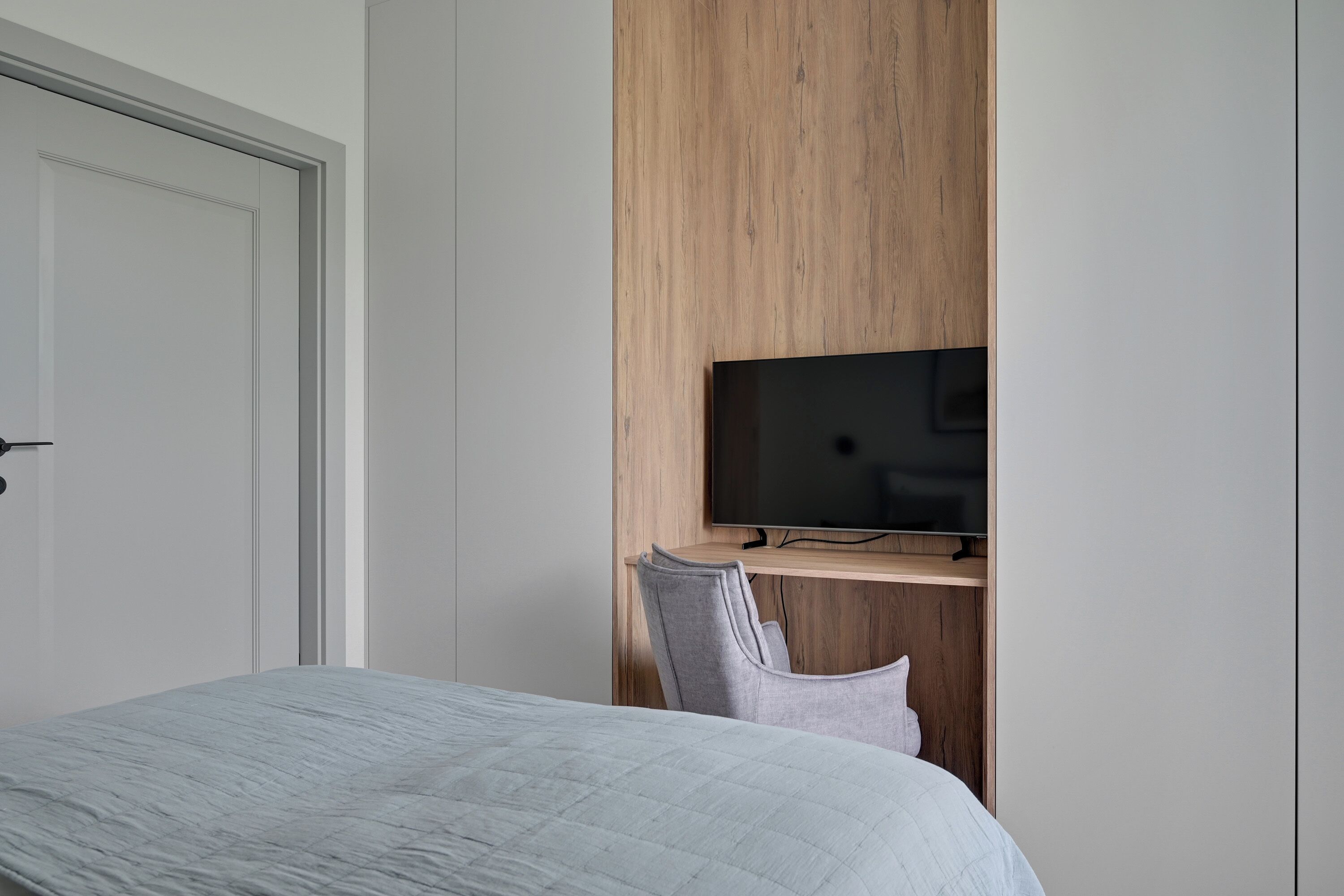 Un dormitorio con una cama, un televisor montado en un panel de madera y una puerta.