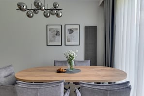 A round dining table with a vase of flowers and a croissant, surrounded by grey upholstered chairs. - Nadmorski Dwór with Parking Sauna & Gym (Gdańsk)
