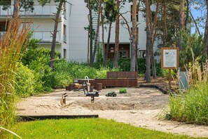 A sandy outdoor area with a wooden bench, a shovel, and a green toy tractor. - Nadmorski Dwór with Parking Sauna & Gym (Gdańsk)