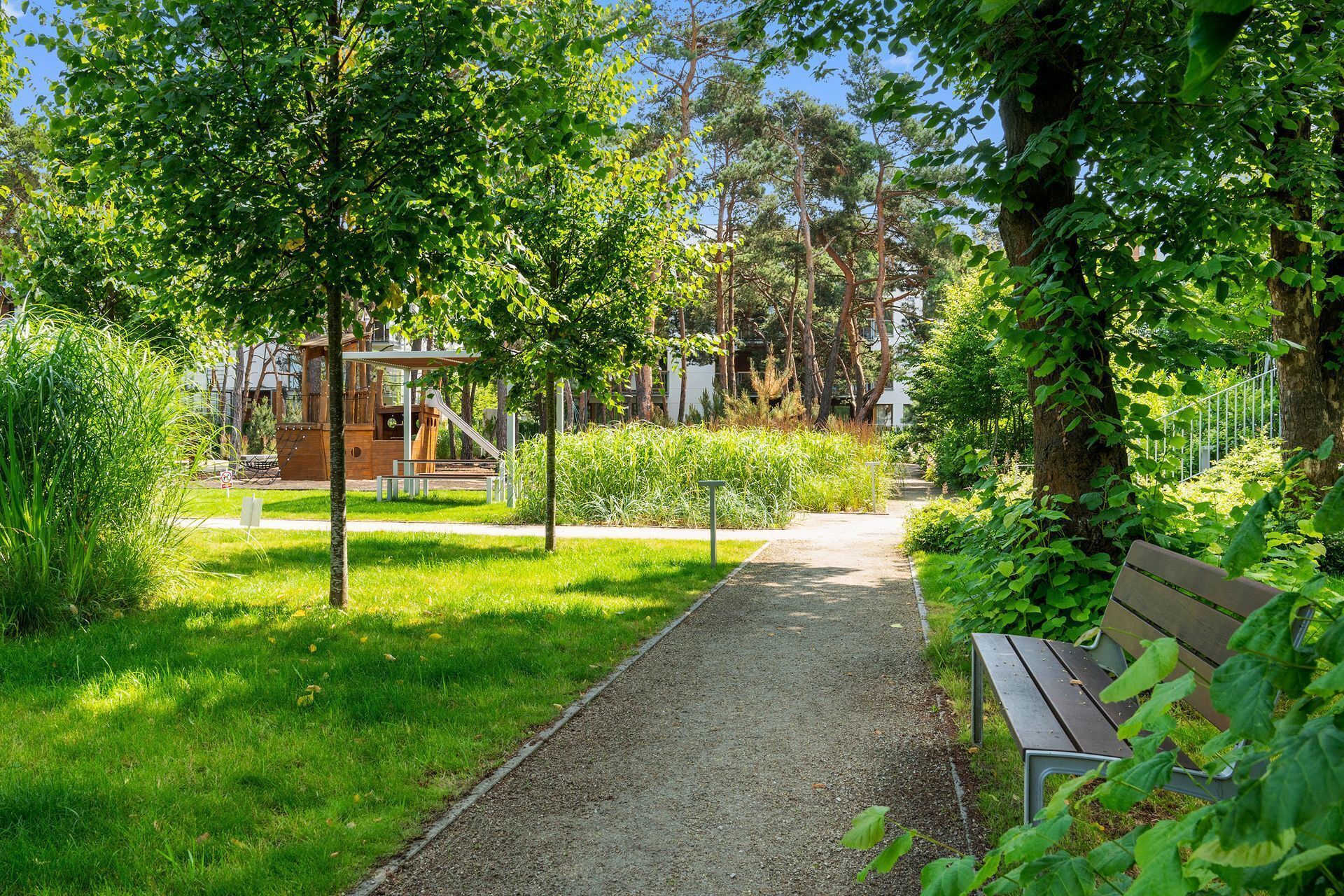 Un vialetto nel parco con una panchina, alberi e un'area giochi.